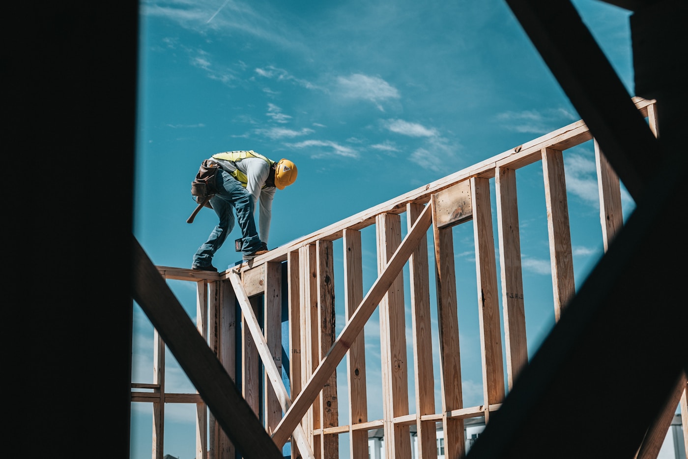 A framer working on a wood-frame structure against a clear blue sky